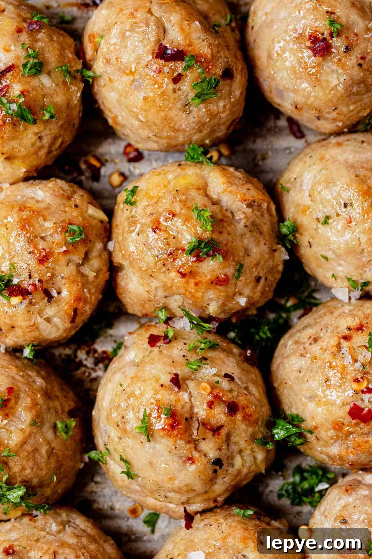 Oven-Baked Turkey Meatballs with Savory Herb Sauce 9 homemade baked turkey meatballs on a sheet pan with fresh parsley.