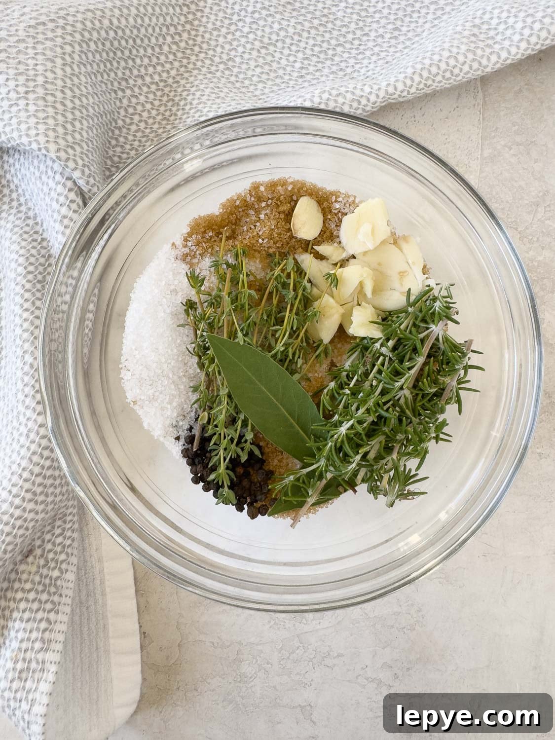 Salt, brown sugar, bay leaf, herbs, garlic and peppercorns for pork brine in a bowl.
