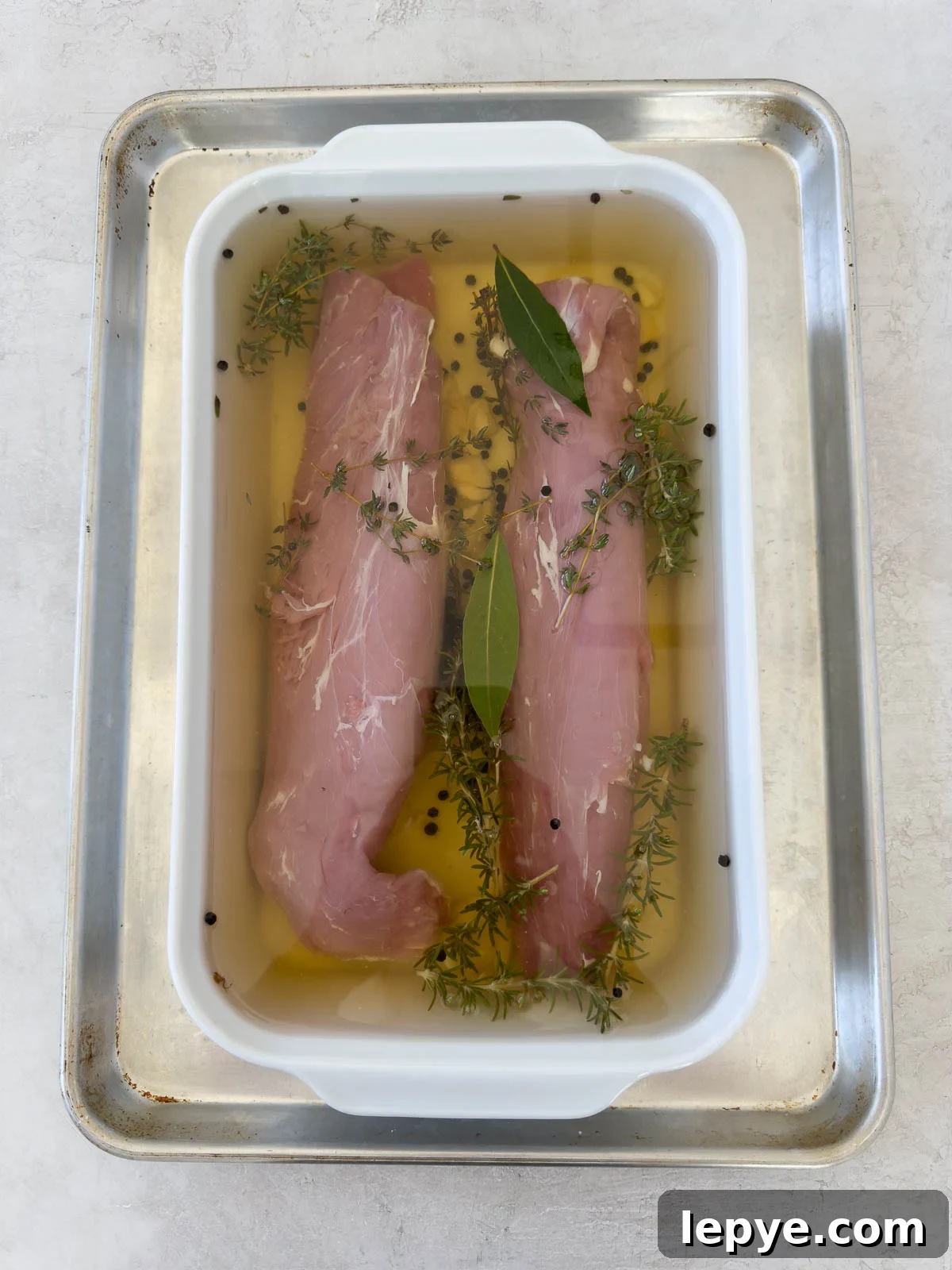 Two pork tenderloins submerged in a pork brine in a shallow casserole dish.