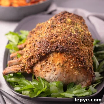 A golden crusted pork rib roast on a gray platter with fresh green parsley.