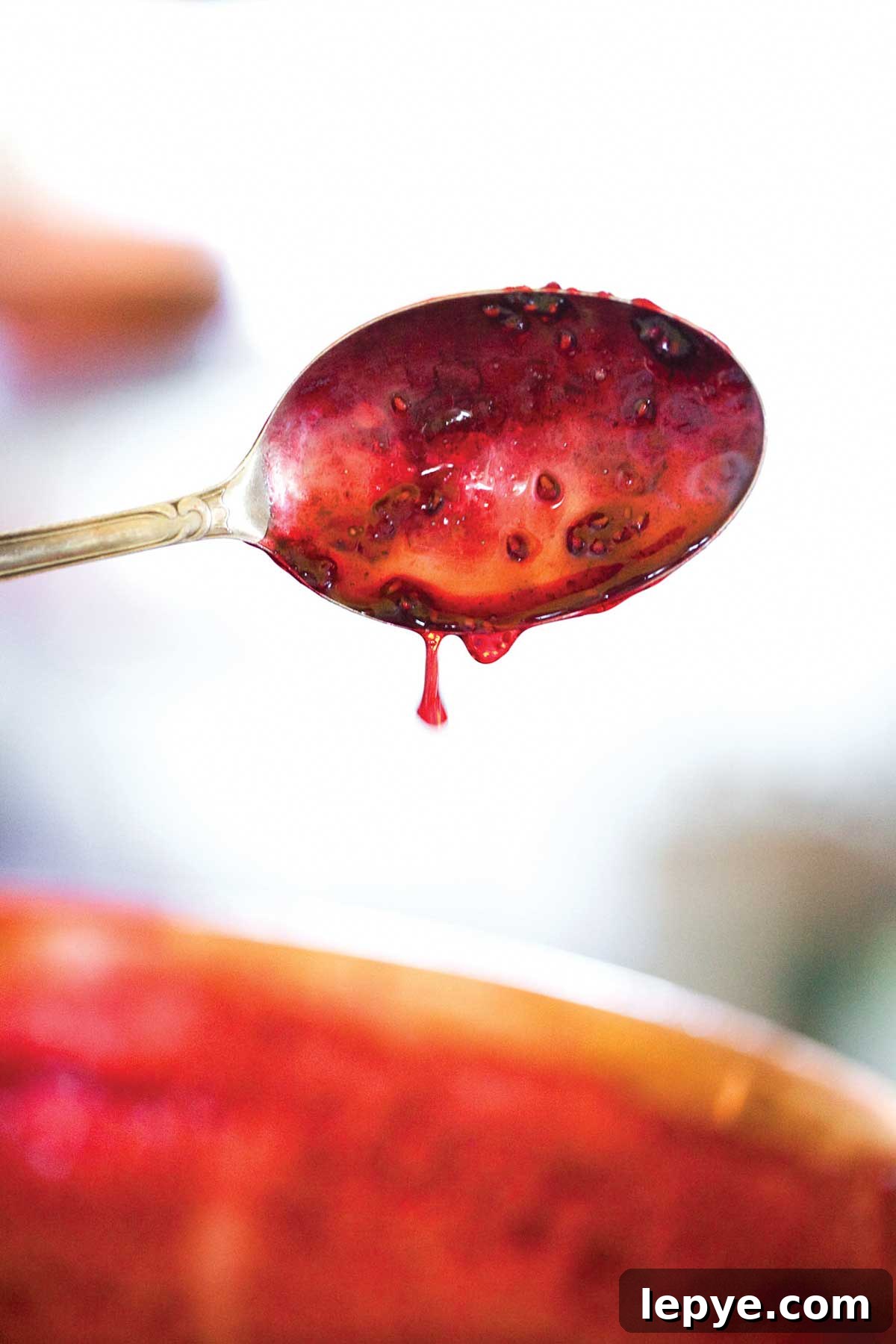 A spoon with raspberry jam dripping off of it.