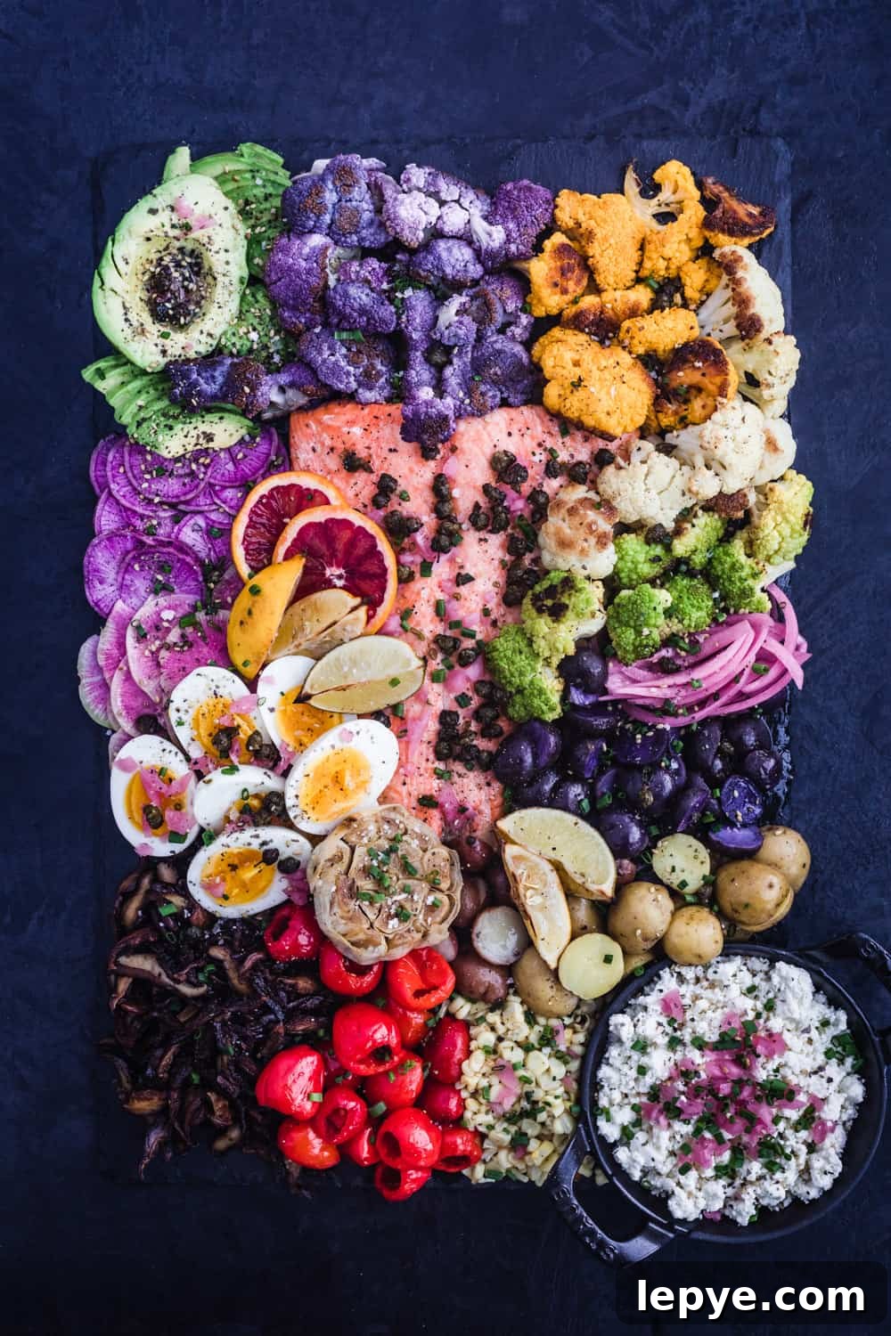 Vibrant Salmon Rainbow Salad Board for Entertaining 3 Salmon Rainbow Party Salad Board with avocado, purple, white, green and yellow cauliflower, pickled red onions, purple and white potatoes, corn, cheese, peppers, garlic, mushrooms, soft boiled eggs, ninja and watermelon radishes, blog oranges, lemons, limes, fried capers and shallots. Overhead shot.