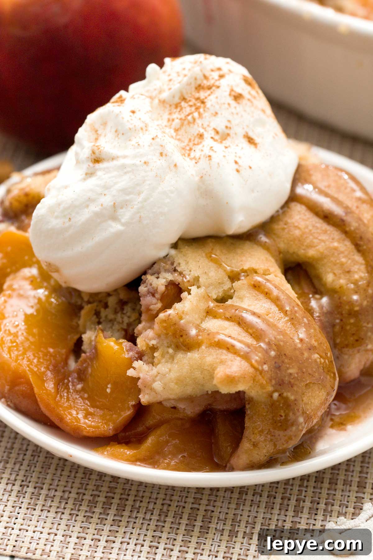 Gluten-Free Peach Cobbler with Almond Butter Caramel Sauce 4 A close-up of gluten-free peach cobbler with oat and almond flour and whipped cream on top.