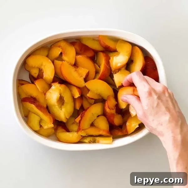 Gluten-Free Peach Cobbler with Almond Butter Caramel Sauce 6 Spreading sliced peaches out in a bowl.
