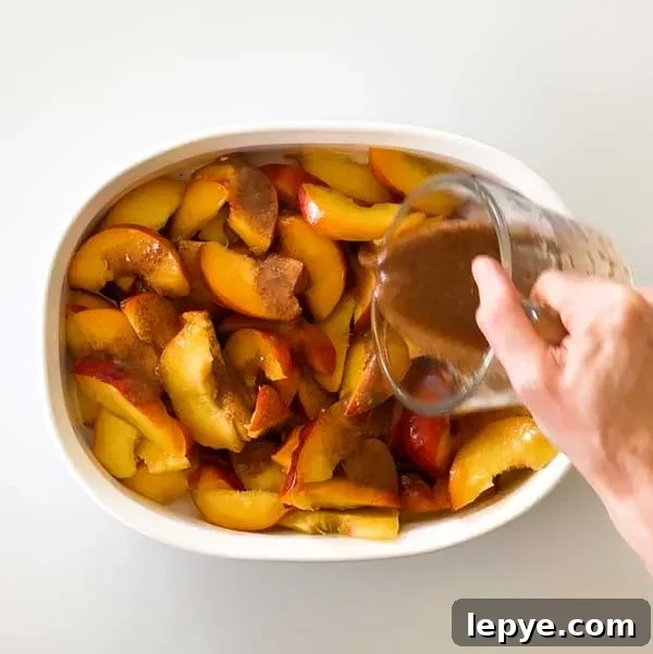 Gluten-Free Peach Cobbler with Almond Butter Caramel Sauce 9 Pouring the cinnamon mixture over the sliced peaches in a shallow white dish.