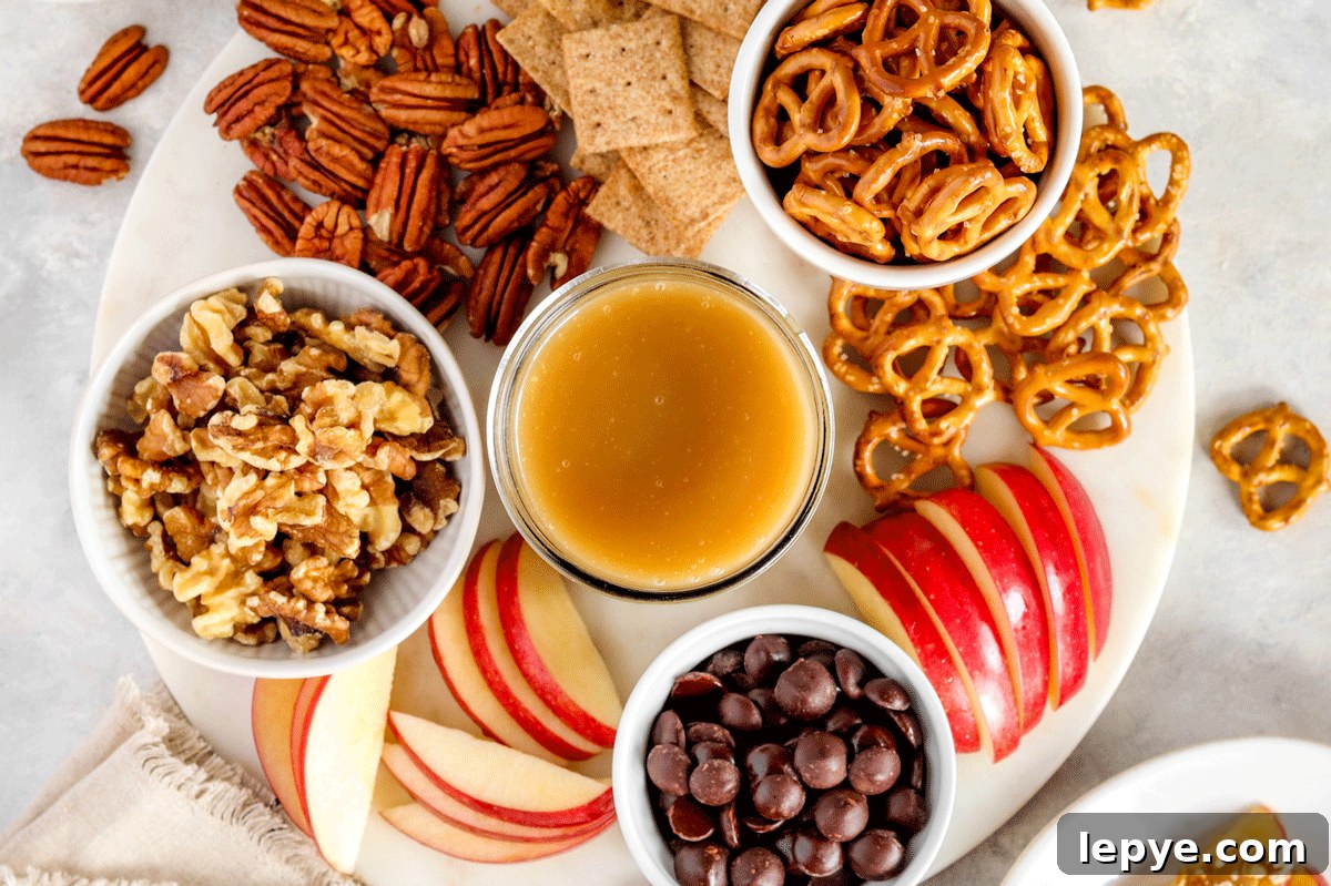 DIY Smooth Caramel Dip Recipe Without Condensed Milk 5 caramel dip in a jar on a charcuterie board filled with pretzels, chocolate and sliced apples.