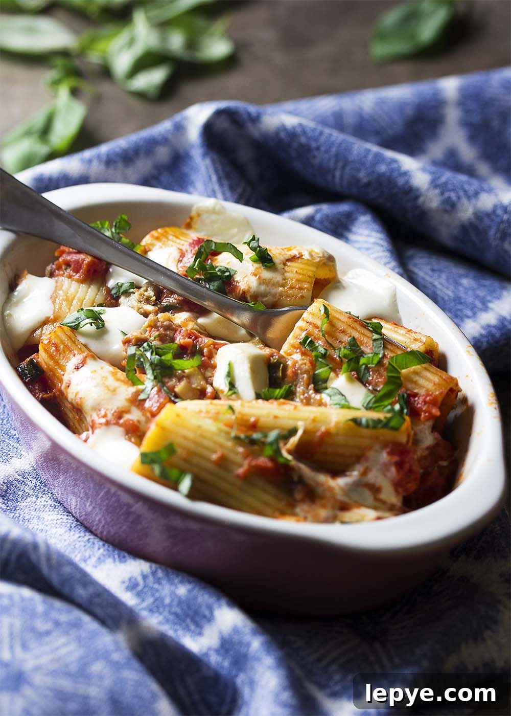 A small dish a sausage pasta al forno with sliced basil and melted mozzarella on top.