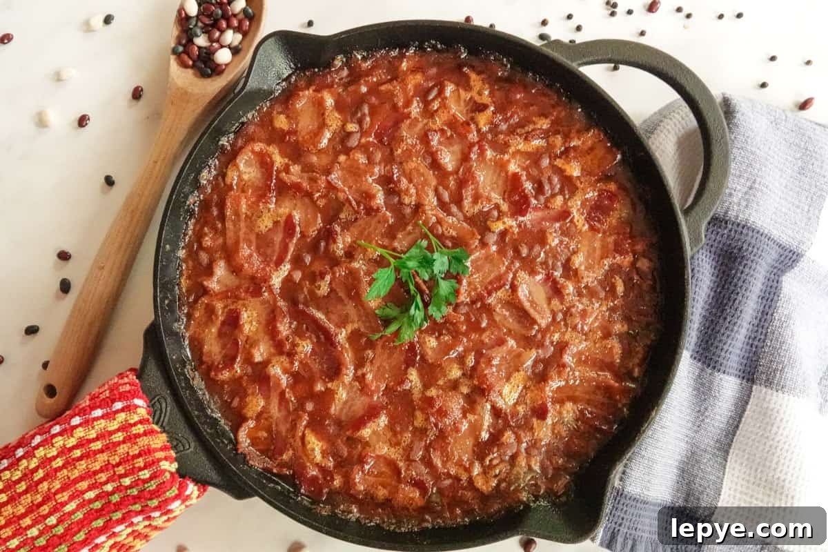 Smoked Baked Beans with Bacon — Flavorful BBQ Side Dish 2 Baked beans in cast iron pan with hand towel