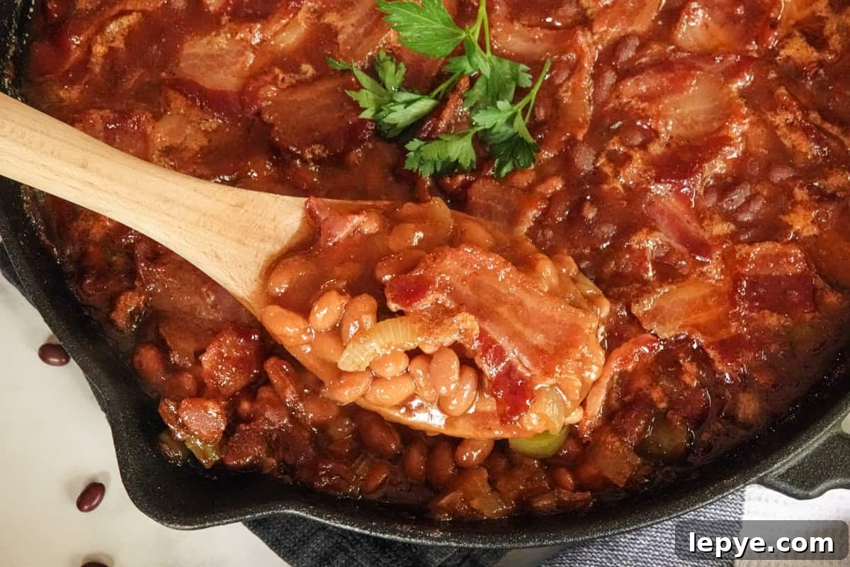 Smoked Baked Beans with Bacon — Flavorful BBQ Side Dish 9 Baked beans being spooned out of pan