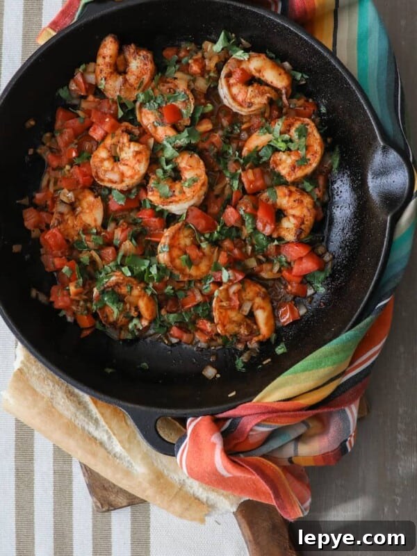 Mexican Shrimp Cocktail Recipe: Zesty Camarones en Coctel 12 Cast iron skillet filled with camarones a la mexicana, featuring shrimp sautéed with tomatoes, onions, jalapeños, and fresh cilantro, served with crusty bread and a colorful striped kitchen towel.