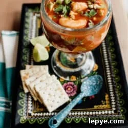 Mexican Shrimp Cocktail Recipe: Zesty Camarones en Coctel 13 Mexican shrimp cocktail (coctel de camarones) served in a large goblet with shrimp, avocado, and cilantro in a tomato-based sauce, on a black plate with saltine crackers