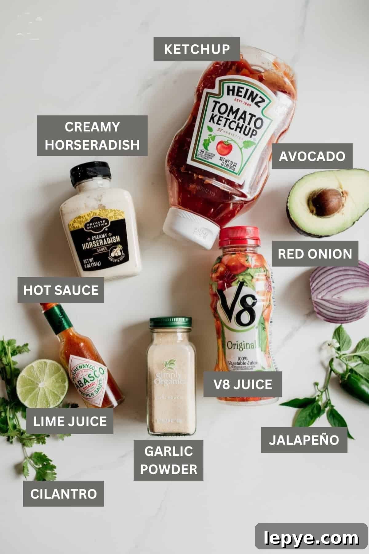 Mexican Shrimp Cocktail Recipe: Zesty Camarones en Coctel 5 Ingredients for Coctel de Camarones (Mexican Shrimp Cocktail) including creamy horseradish, ketchup, V8 vegetable juice, hot sauce, garlic powder, red onion, avocado, lime, cilantro, and jalapeno on a white surface