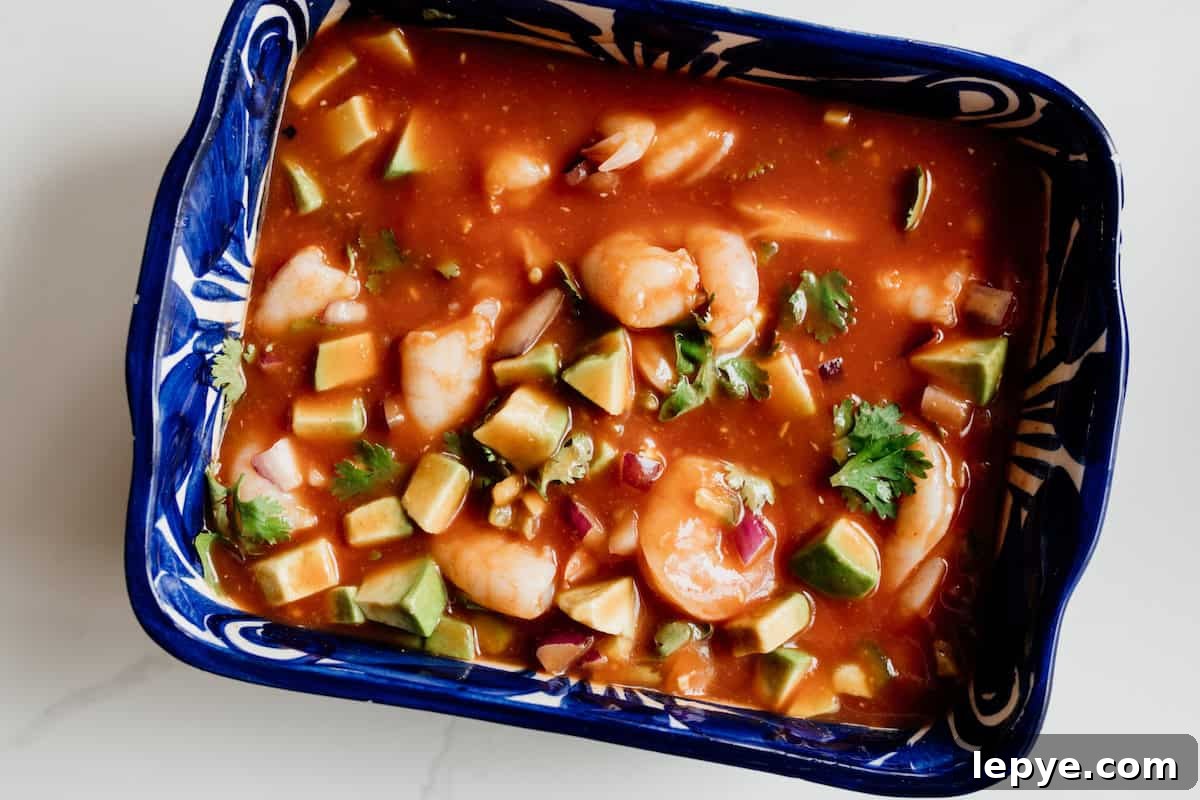 Mexican Shrimp Cocktail Recipe: Zesty Camarones en Coctel 7 Completed Coctel de Camarones (Mexican shrimp cocktail) served in a rectangular blue bowl, garnished with avocado and cilantro, ready to serve family-style