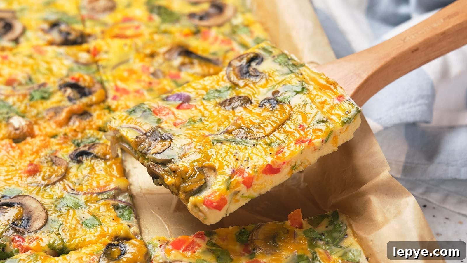 15 High-Protein Breakfasts to Power Your Morning Hustle 2 A square slice of sheet pan omelet on a wooden spatula above parchment paper.