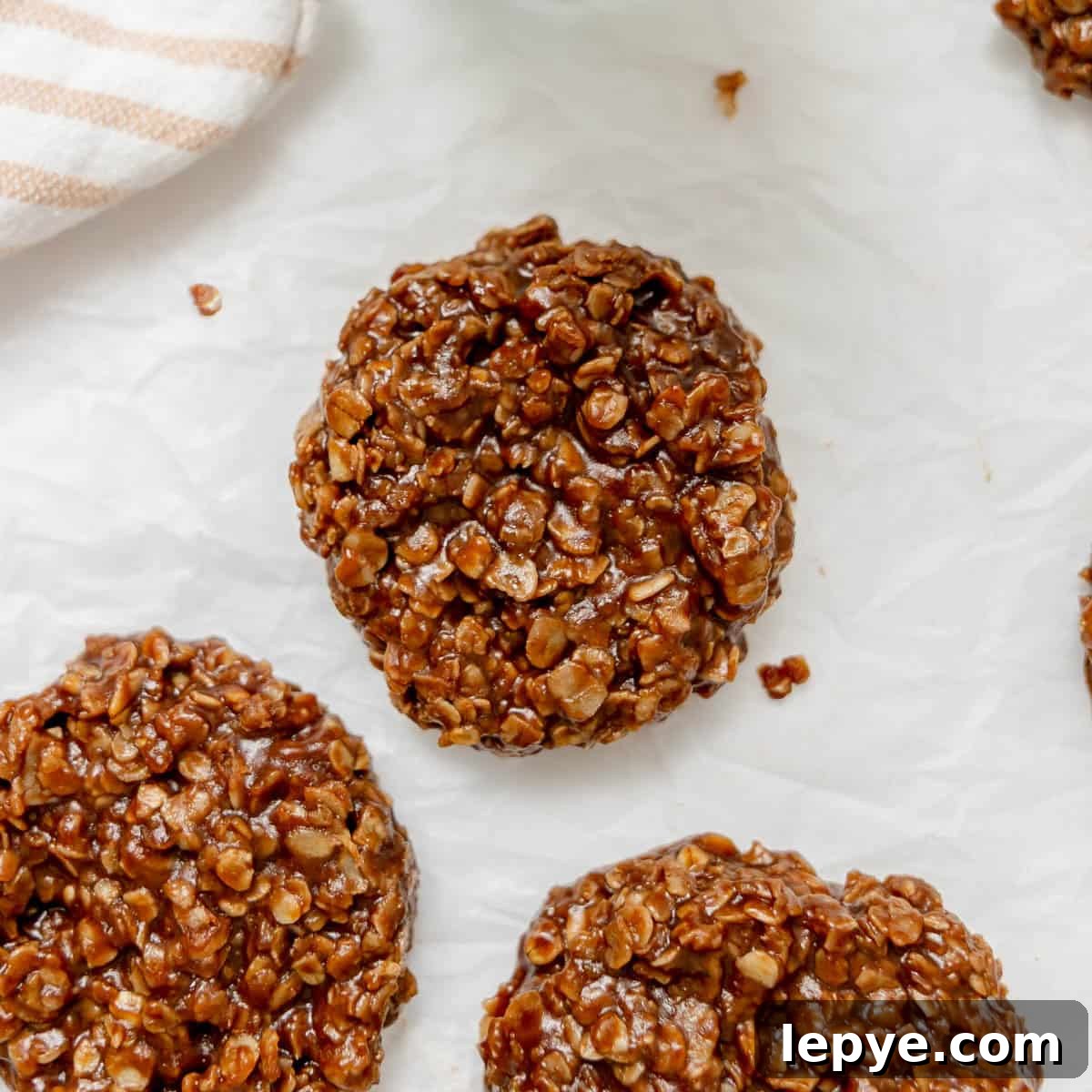 Chocolate oatmeal no-bake cookies arranged on white parchment paper, with part of a striped cloth visible in the corner.