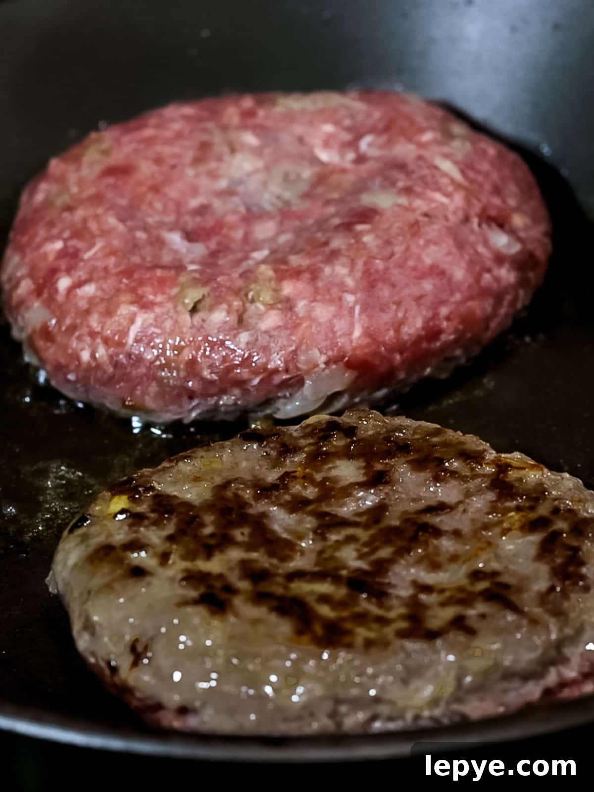 Japanese hamburger steak patties cooking in a pan with golden brown edges.