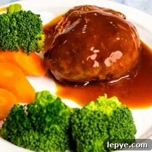 Japanese hamburger steak (hambāgu ハンバーグ) on a white plate next to broccoli and carrots.