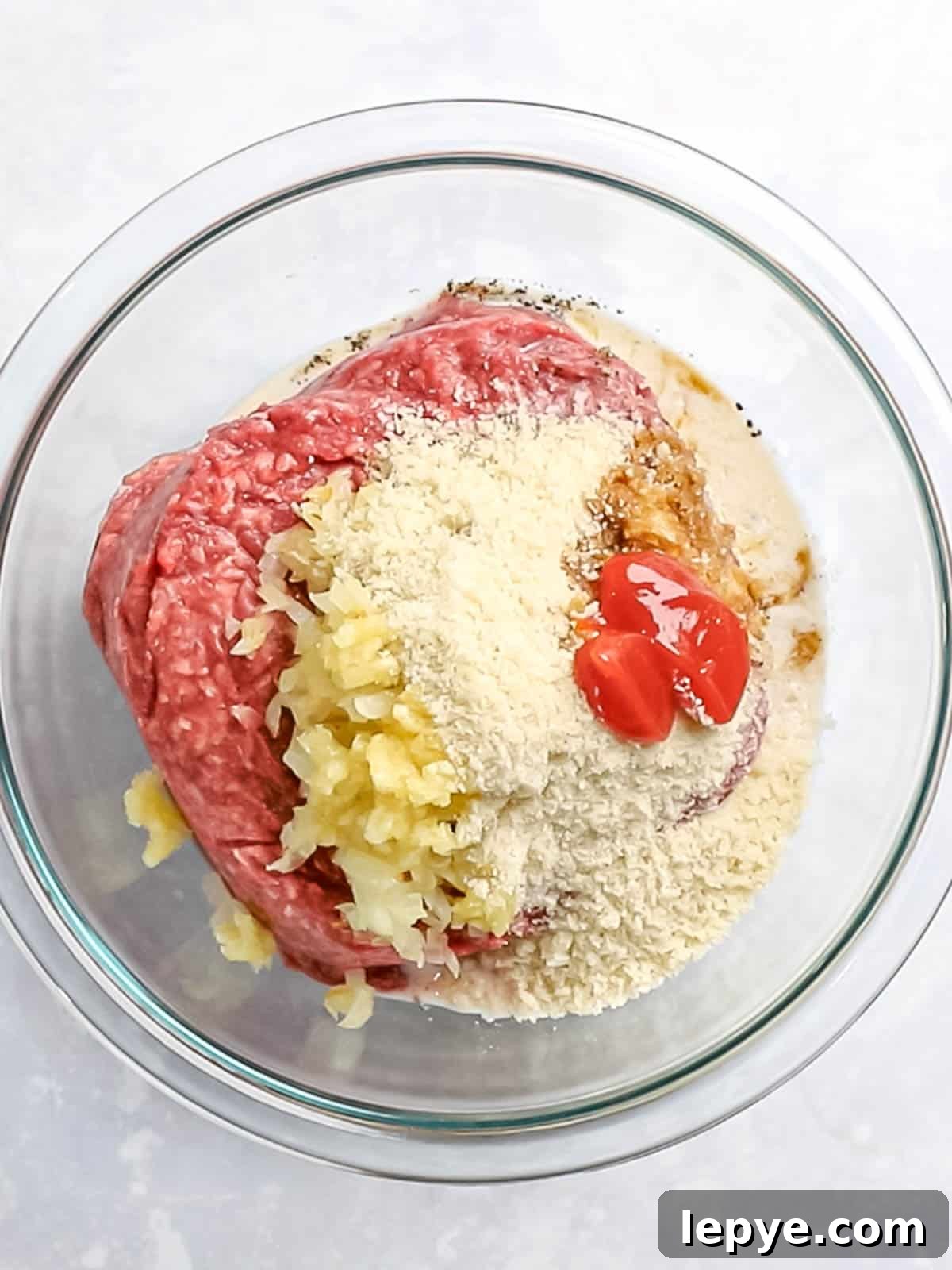 Ground beef, panko, onions, and ketchup in a glass bowl.