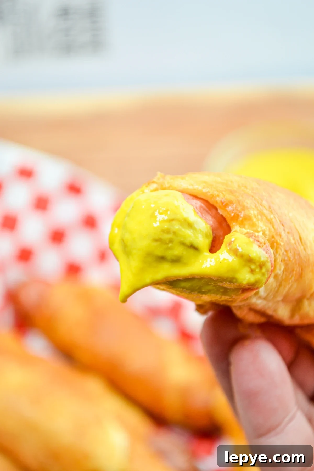 Crispy Air Fryer Pigs in a Blanket Recipe 3 A pig in a blanket, dipped in bright yellow mustard.