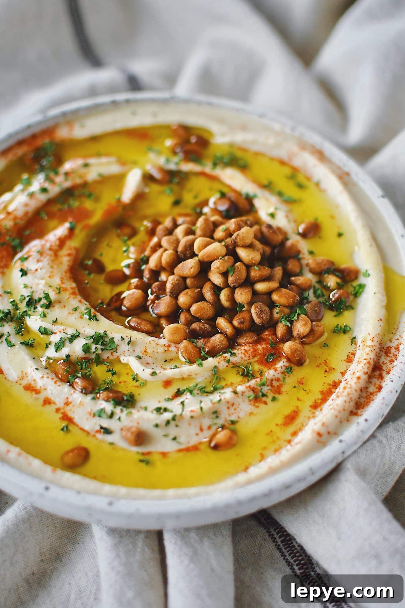 Homemade Hummus, topped with olive oil, paprika, toasted pine nuts, and parsley, ready to eat.