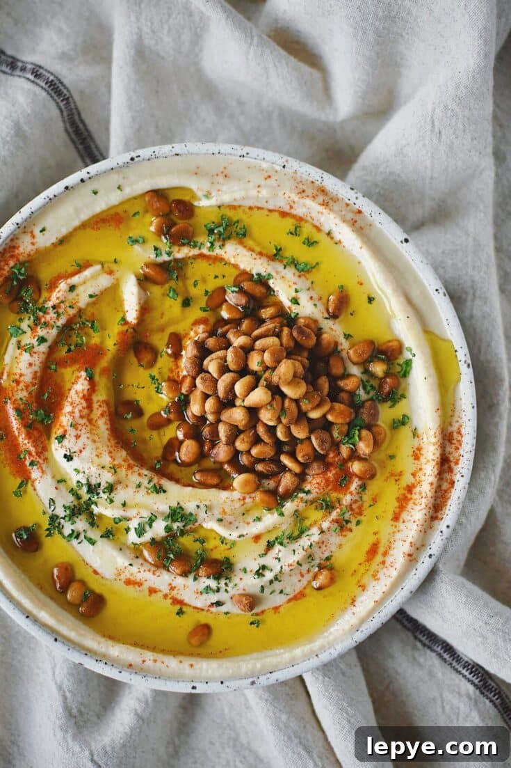 Homemade Hummus, topped with olive oil, paprika, toasted pine nuts, and parsley, ready to eat.