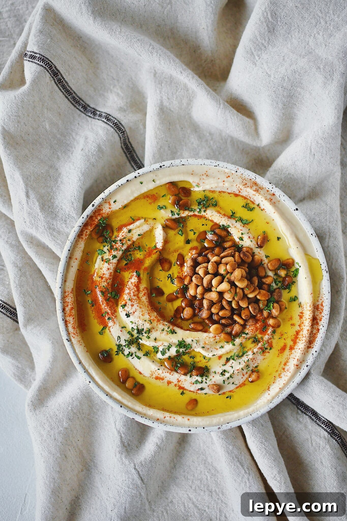 Homemade Hummus, topped with olive oil, paprika, toasted pine nuts, and parsley, ready to eat.