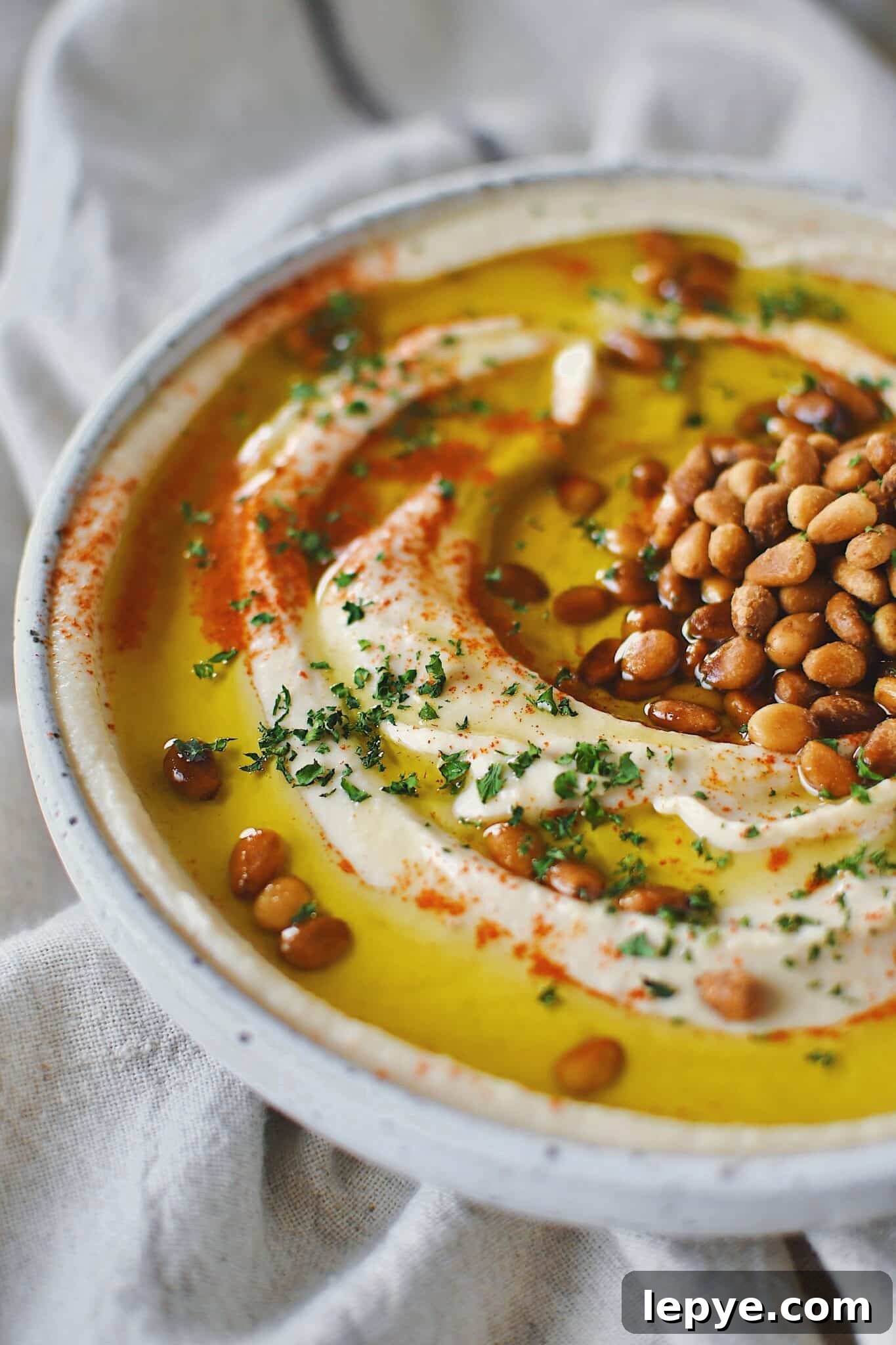 Homemade Hummus, topped with olive oil, paprika, toasted pine nuts, and parsley, ready to eat.