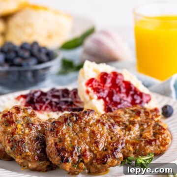 A plate of homemade breakfast sausage patties with a biscuit, jam, and a glass of orange juice