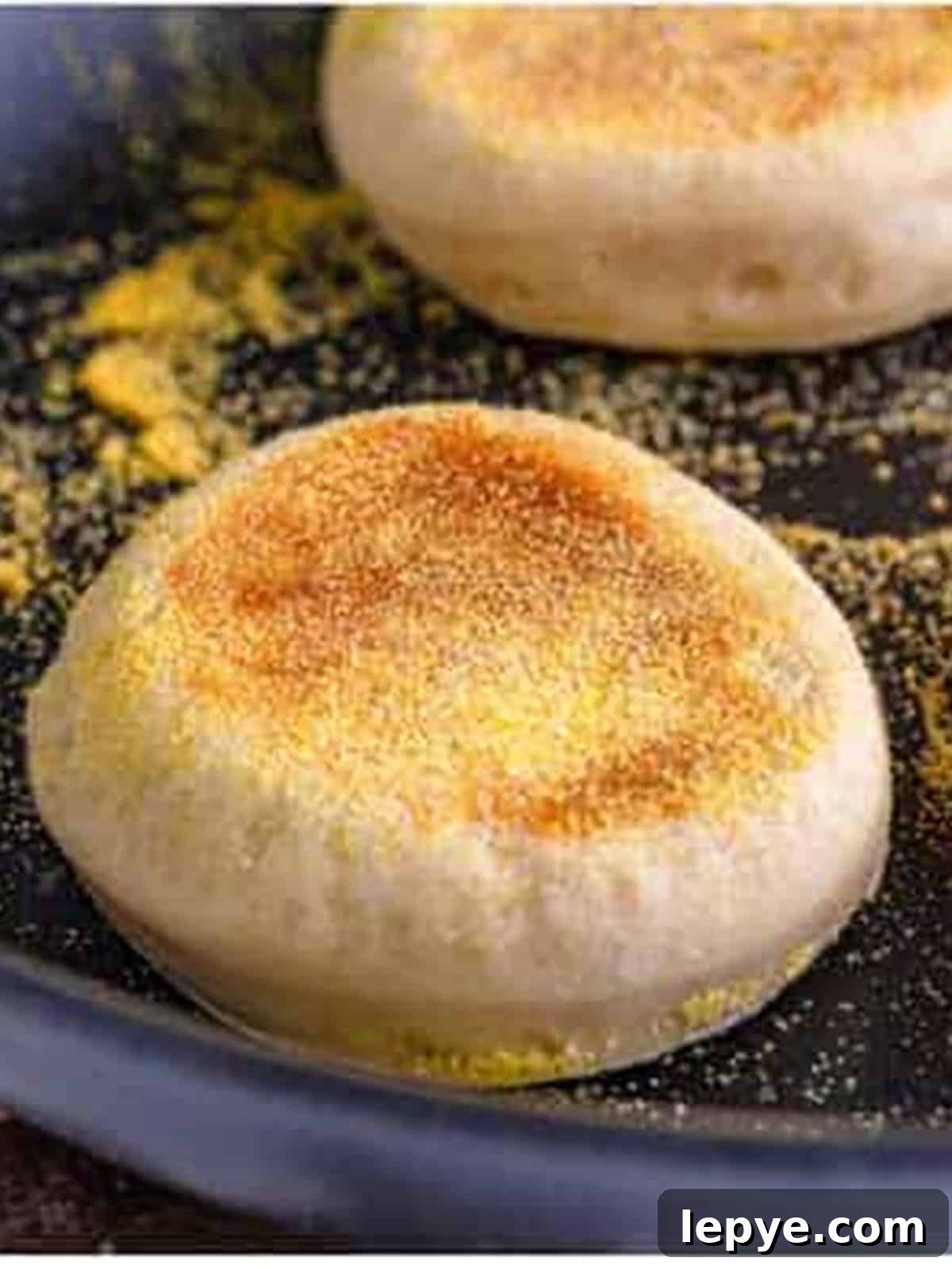 English muffins cooking golden brown in a cornmeal-dusted skillet.