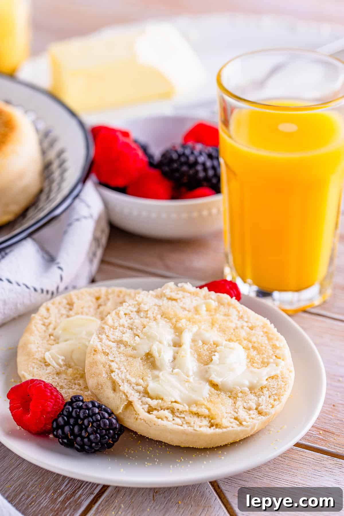 A split English muffin spread with butter, served with berries and orange juice.