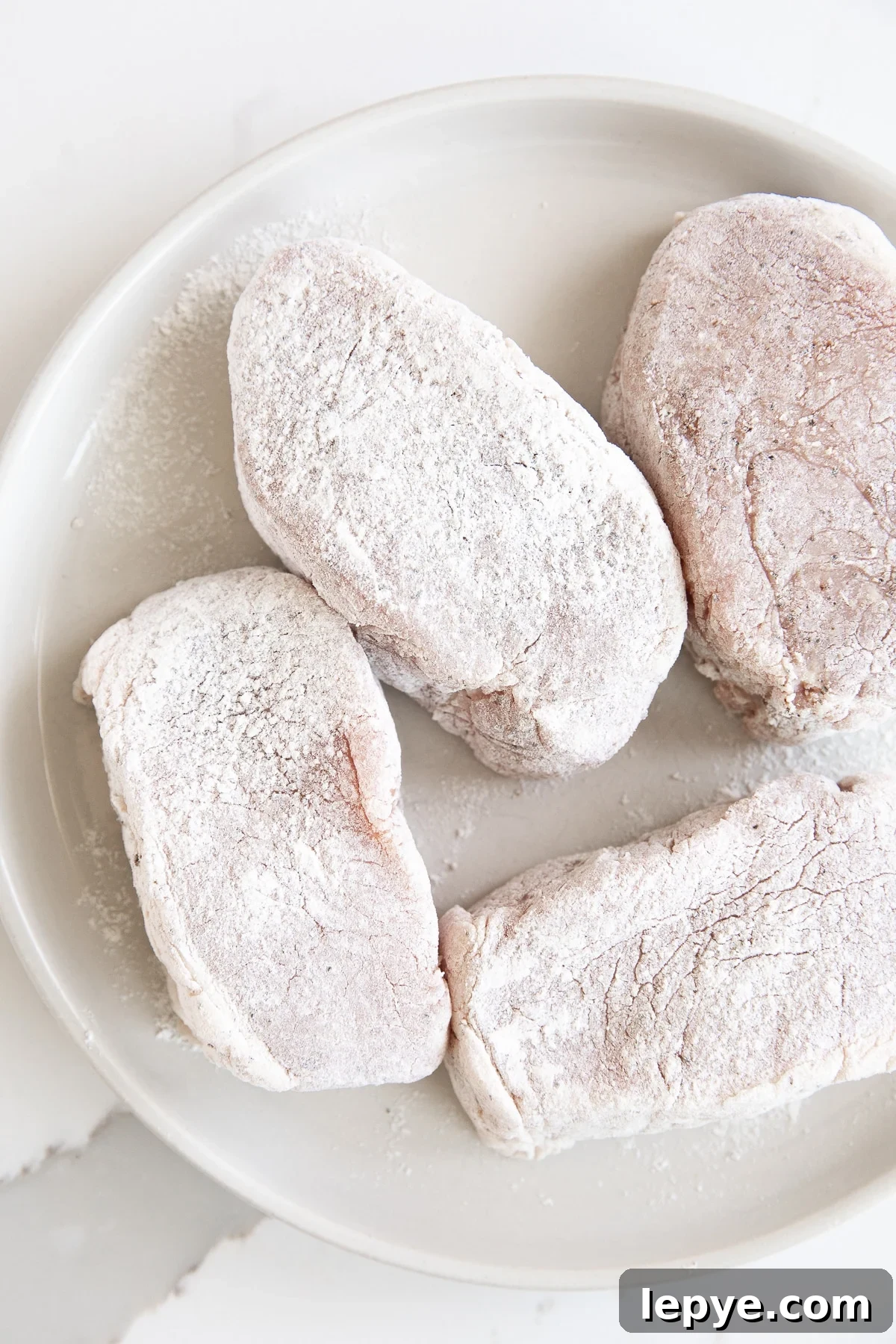 Image of four thick-cut boneless pork chops coated with flour.
