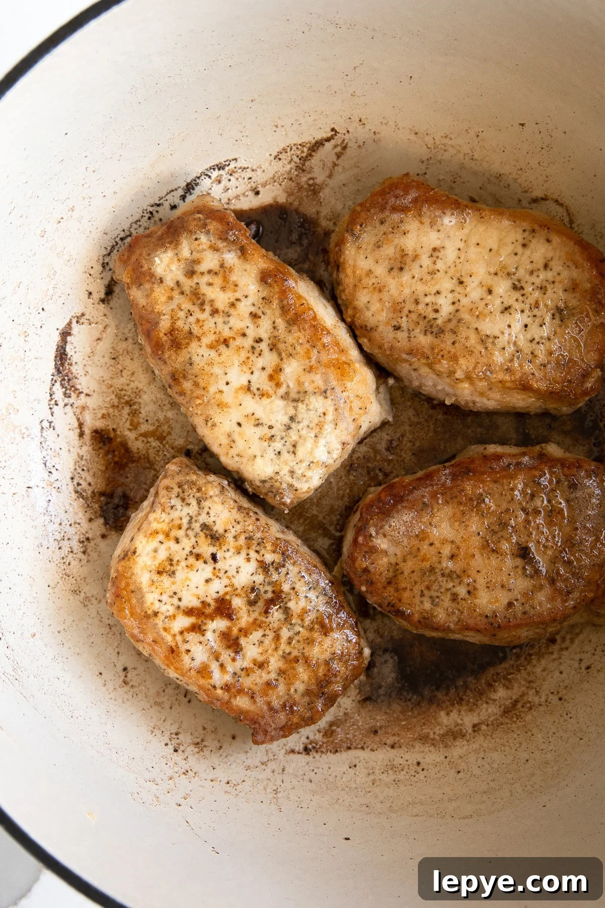 Image of four seared pork chops in a large Dutch oven.