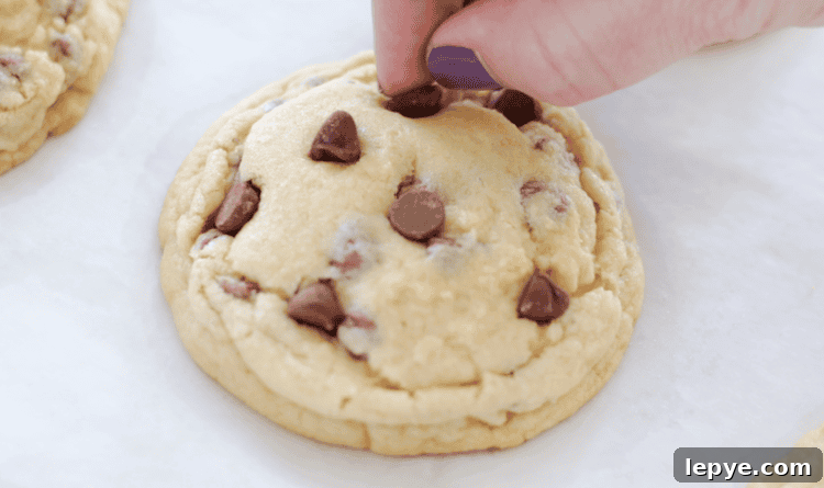 hand adding additional chocolate chips onto the top of the baked cookie